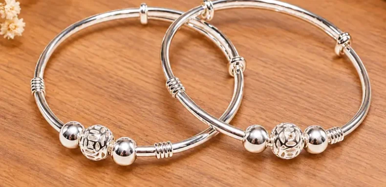 Hai vòng bạc ta trẻ em có ba bi bạc, họa tiết bi kim tiền, chụp trên nền gỗ