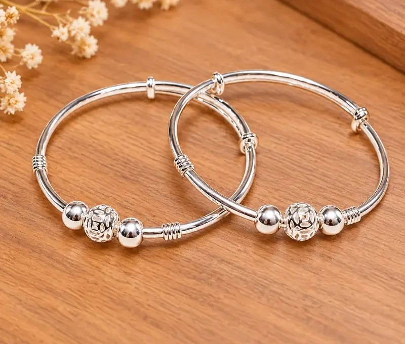 Hai vòng bạc ta trẻ em có ba bi bạc, họa tiết bi kim tiền, chụp trên nền gỗ